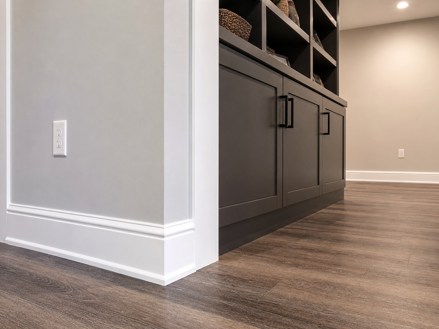 Finished basement trim, built-in storage, baseboard, drywall, and plank flooring detail