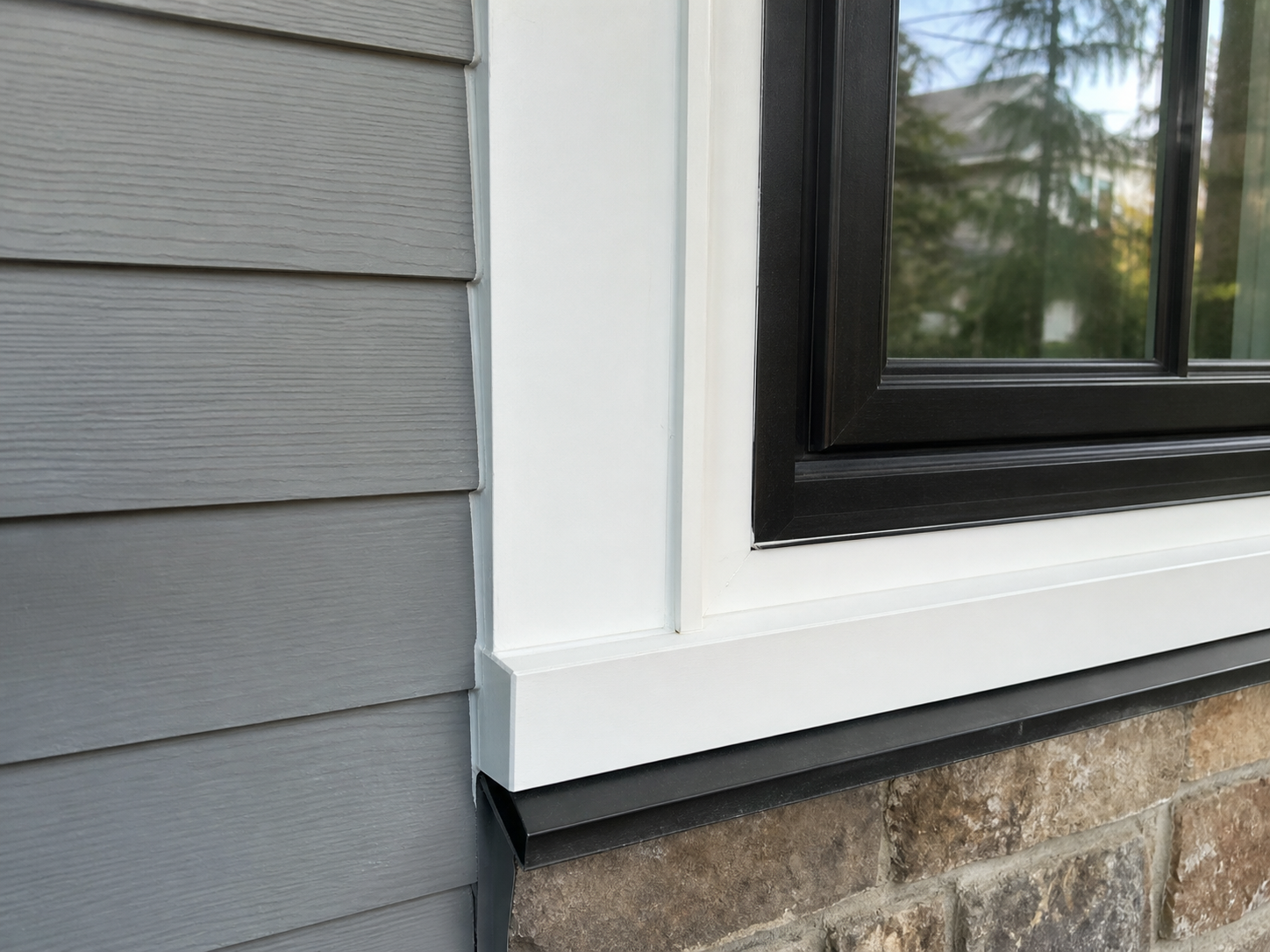 Close detail of replacement window trim, sill flashing, siding, and black window frame
